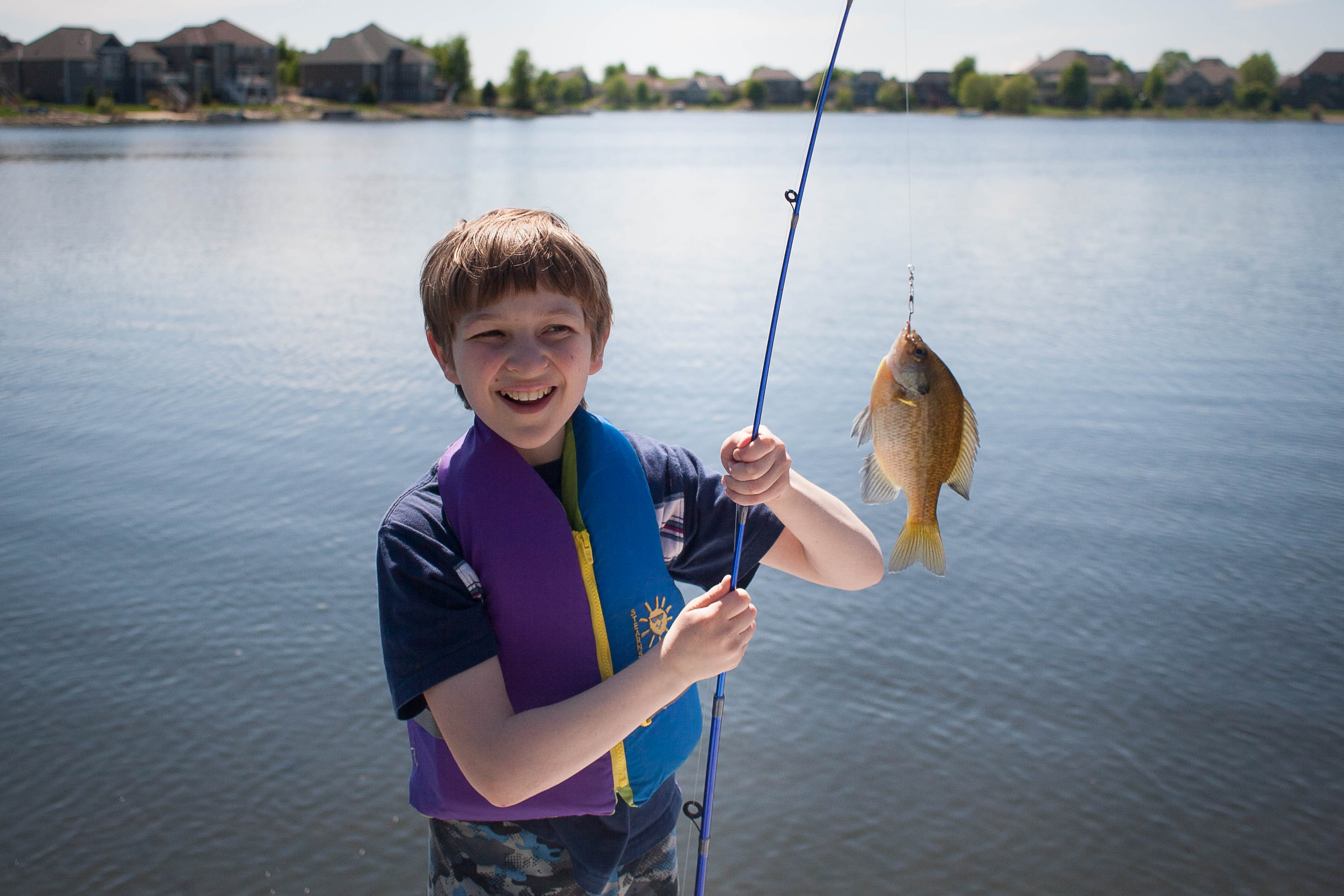 A boy wearing a life jacket smiling at a fish he just caught