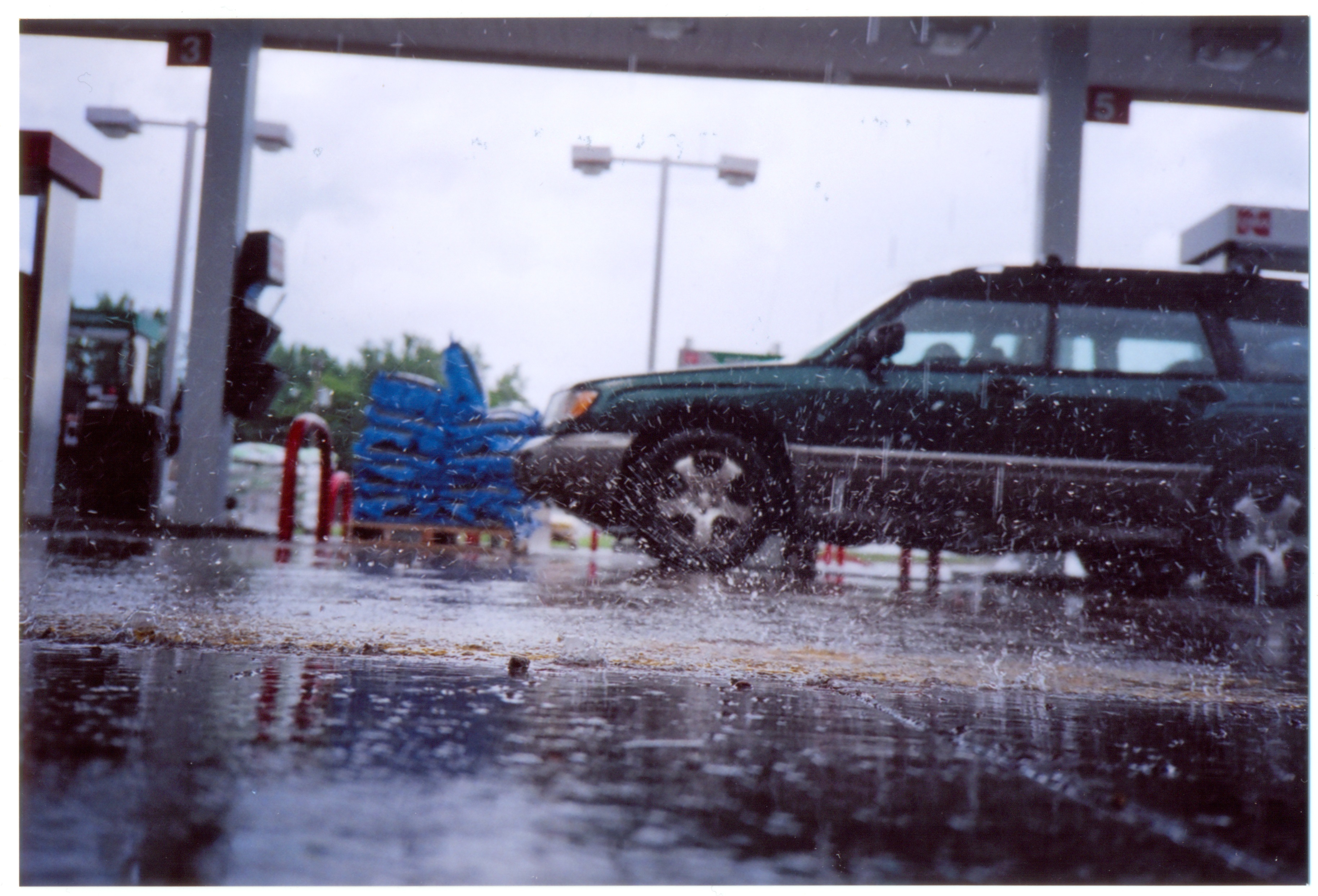 Low angle photograph of raindrops splashing on the pavement at a gas station. My Subaru is in the background of the picture.