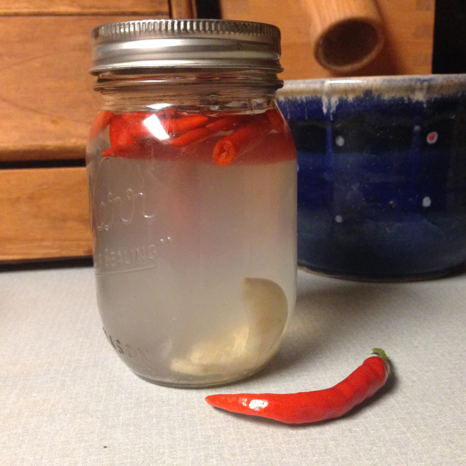 A jar of hot Thai chilis in water, next to another chili sitting on the counter