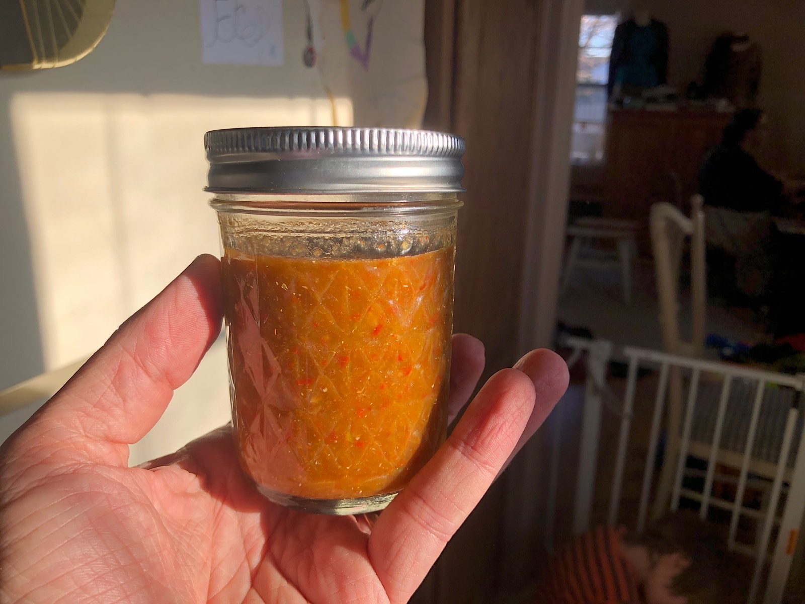 A jar of finished hot sauce, reddish brown in the light