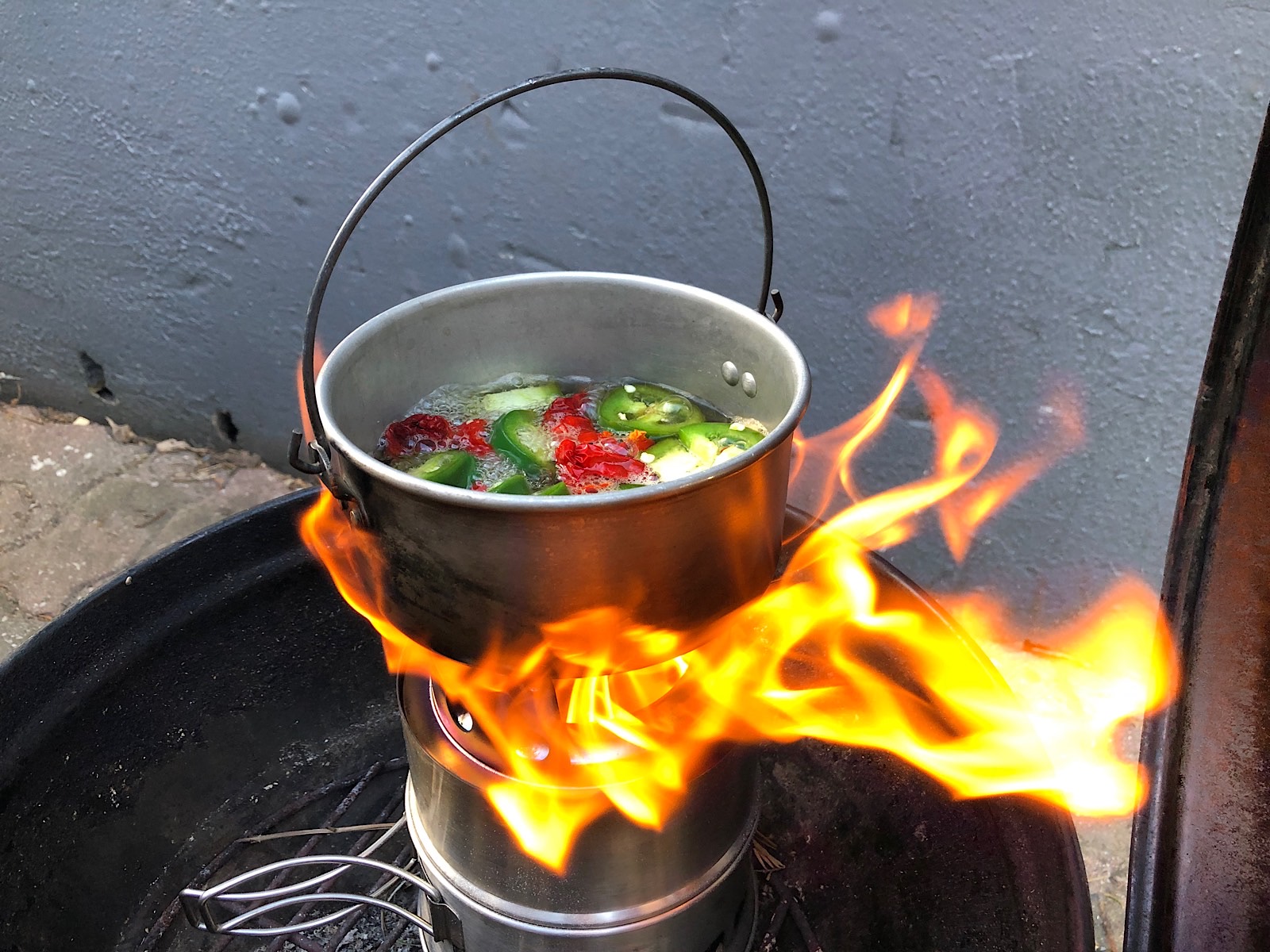 Flames coming up around a pot of simmering green and red hot peppers 